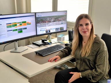 Die Mitarbeiterin Sarah Bibicaj, eine junge Frau mit langen Haaren, sitzt an einem Schreibtisch mit zwei Bildschirmen.